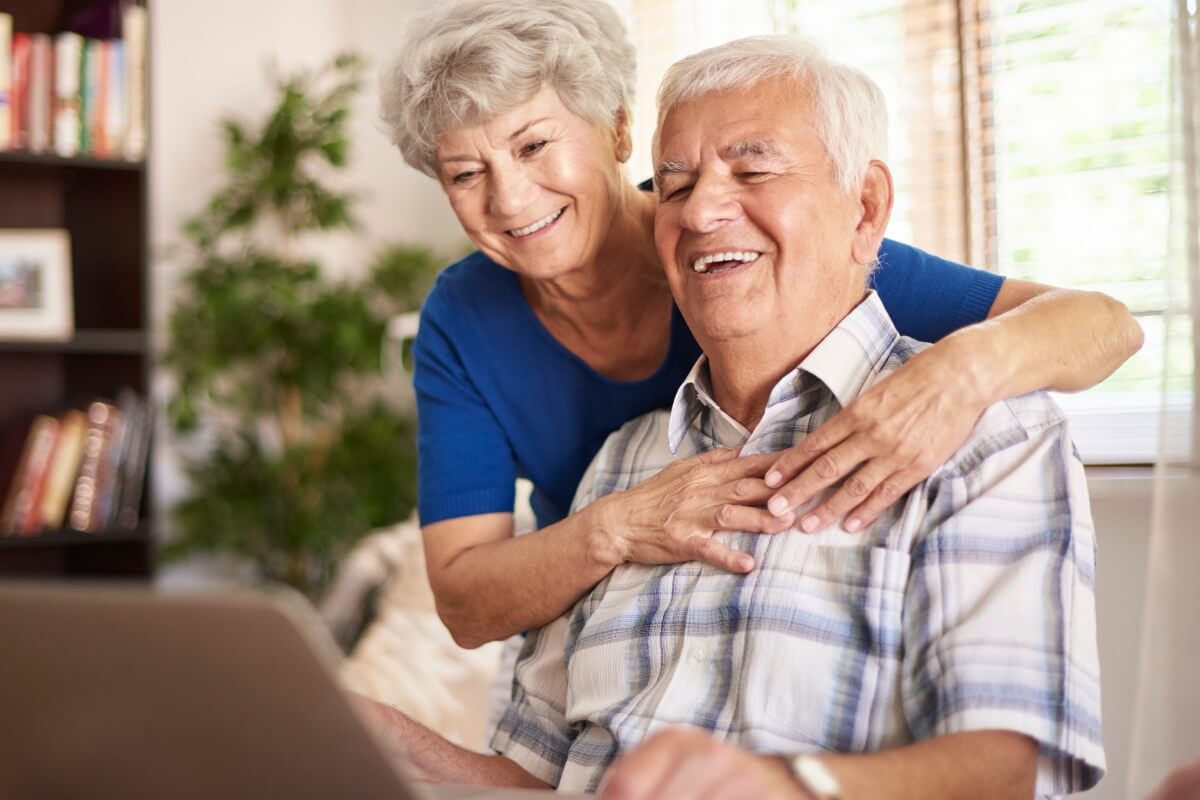 pareja de personas edad mayor sonriendo mirando a un ordenador